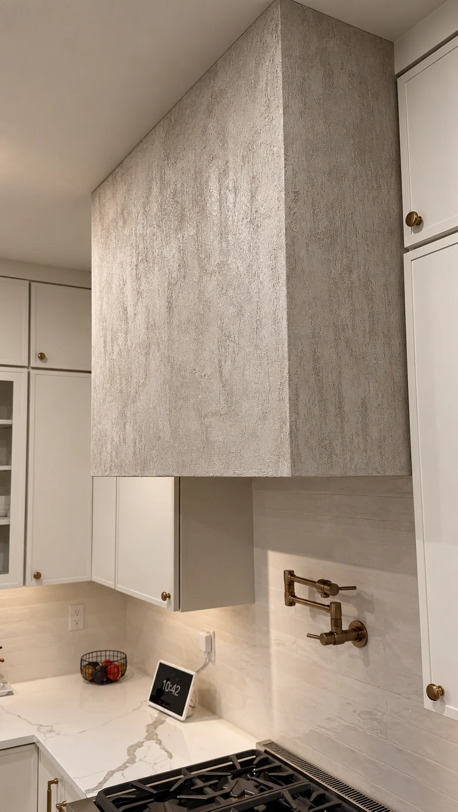 Finished Palladino plaster kitchen hood with travertine-look texture above the range, framed by white cabinetry — Ridgewood, NJ