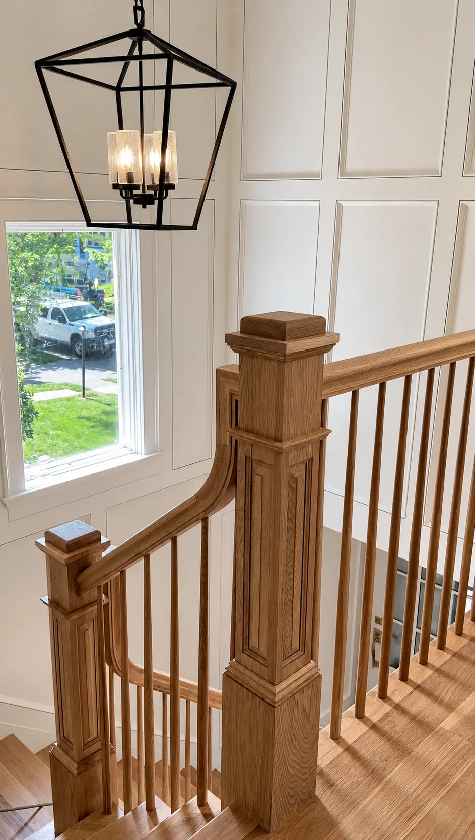 Finished wood staircase with carved newel posts and a geometric pendant light