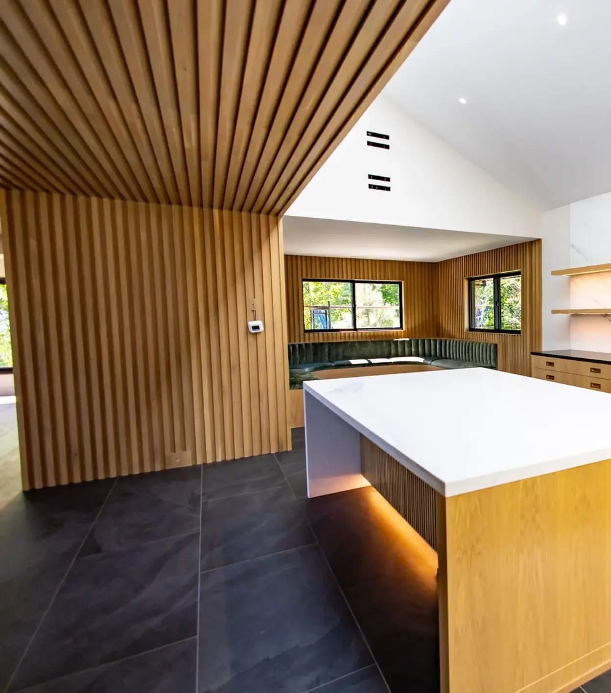Slat wood ceiling and wall above a white marble island with oak base in Pompton Plains, NJ