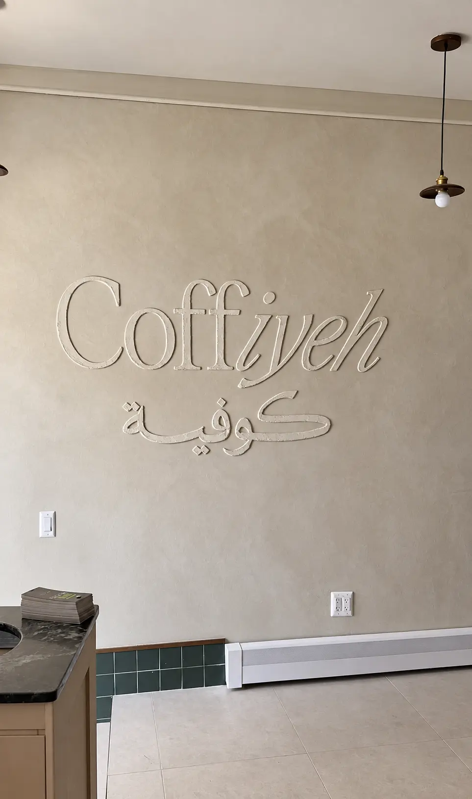 Warm limewash feature wall with raised plaster lettering at Coffiyeh coffee shop in Clifton, NJ