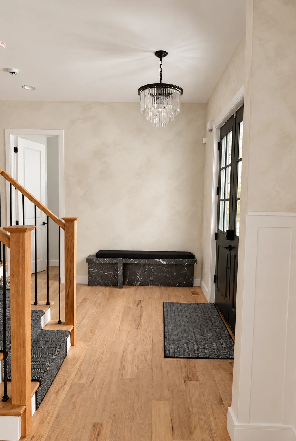 Entry hallway with warm white limewash walls, crystal chandelier and black marble bench in Glen Rock NJ