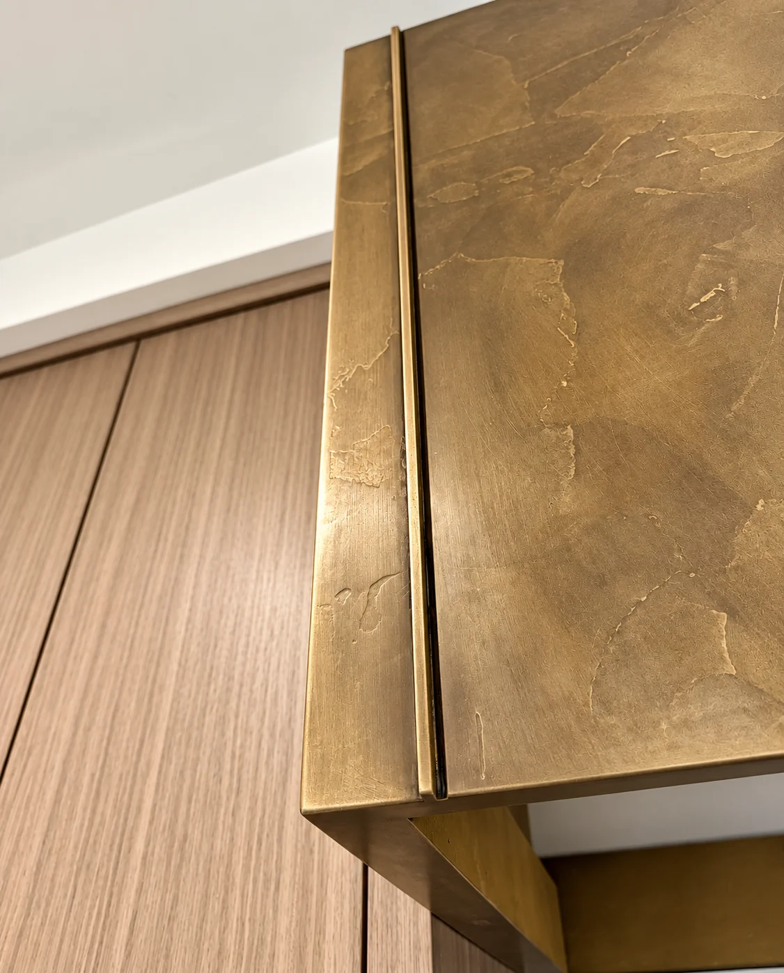 Warm brass-toned metallic plaster finish with organic tonal movement on a panel beside wood-grain cabinetry in Wayne, NJ