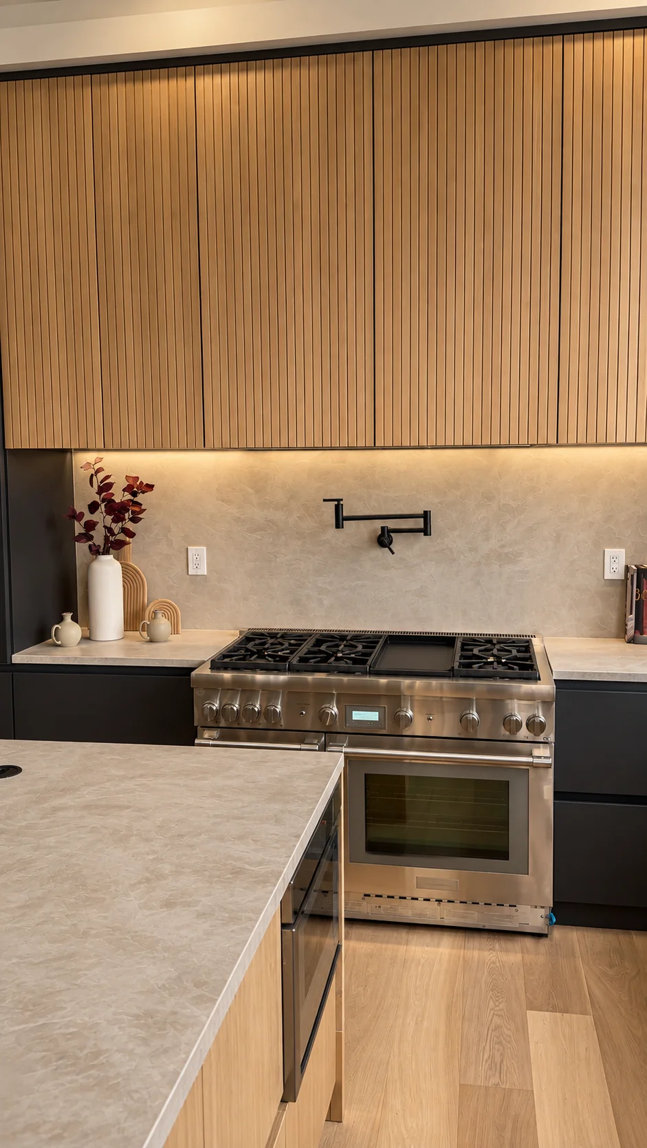 Smooth plaster backsplash behind a professional range with a matte black pot filler, light stone countertops and wood slat cabinets in Paramus, NJ