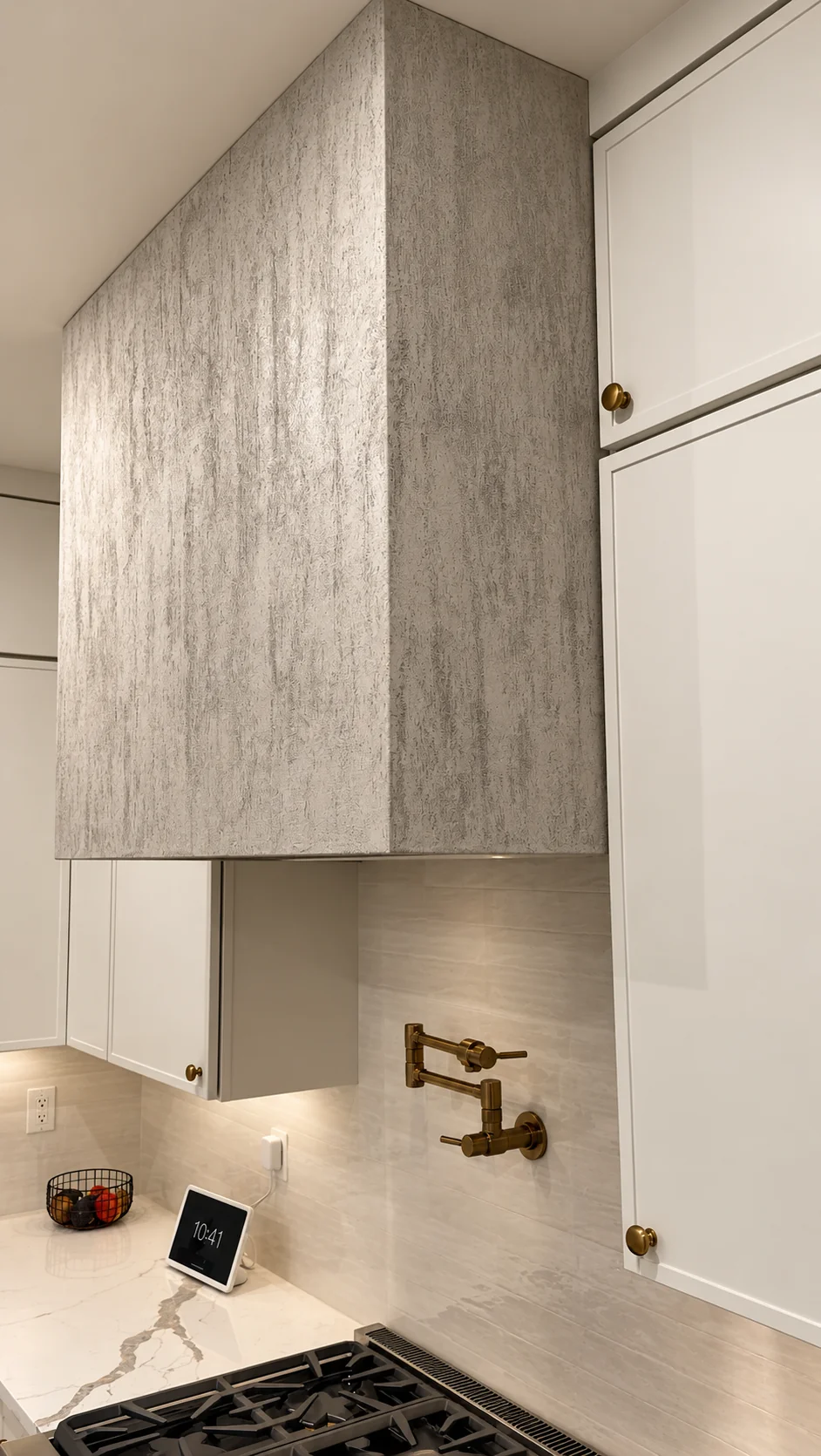 Travertine-look plaster range hood above a tile backsplash with brass pot filler in Ridgewood, NJ
