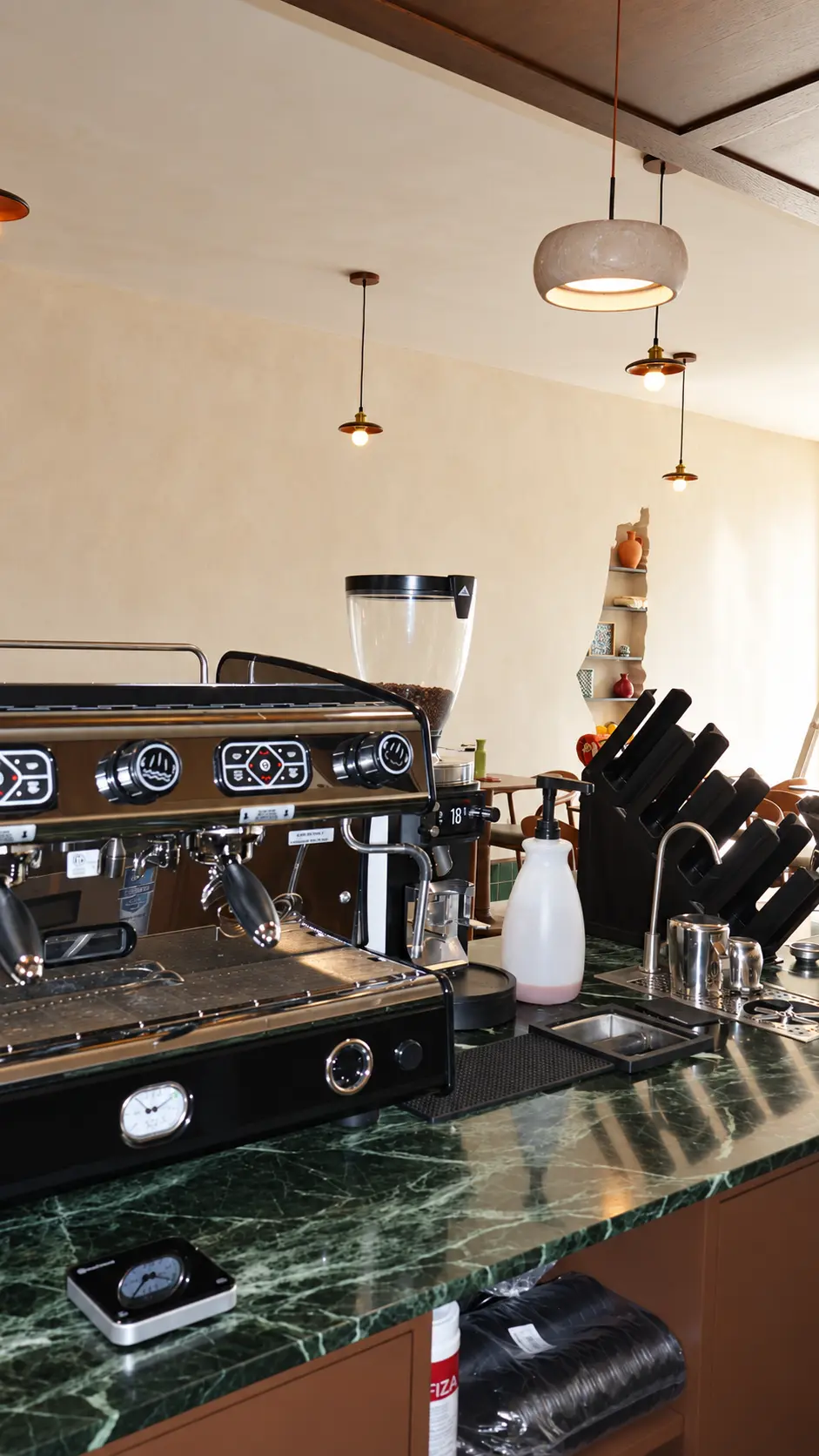 Espresso bar in front of warm limewash walls and ceiling with pendant lights at Coffiyeh coffee shop, Clifton, NJ