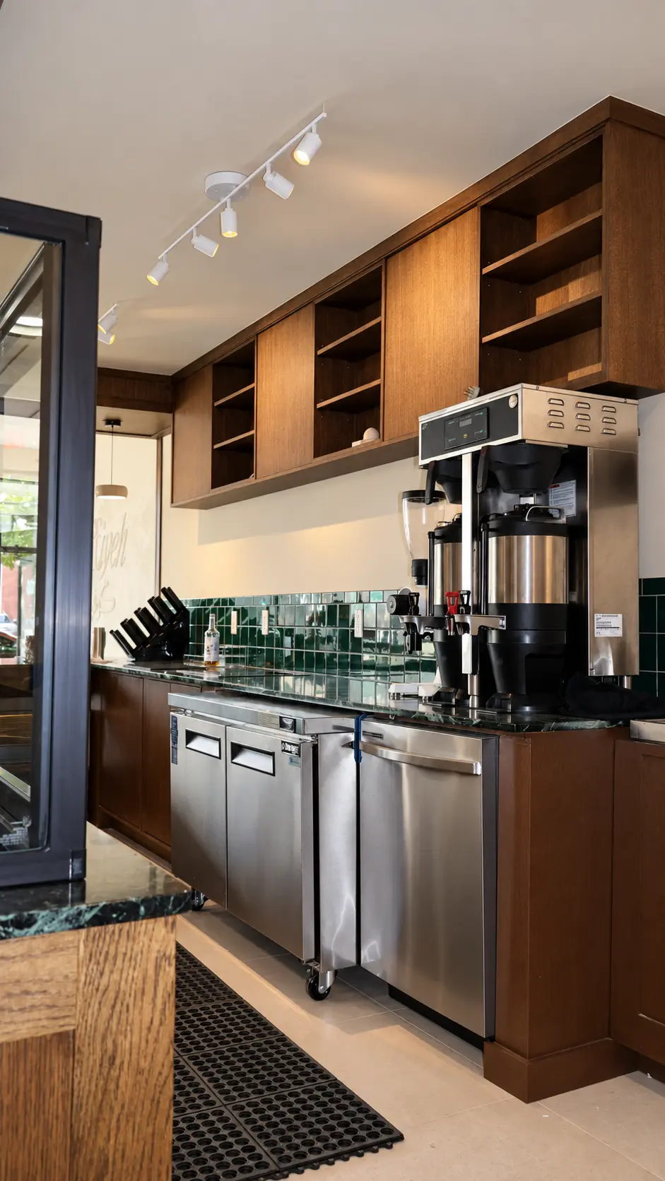 Stained wood cabinetry and open shelving behind the coffee bar with limewash walls at Coffiyeh coffee shop in Clifton, NJ