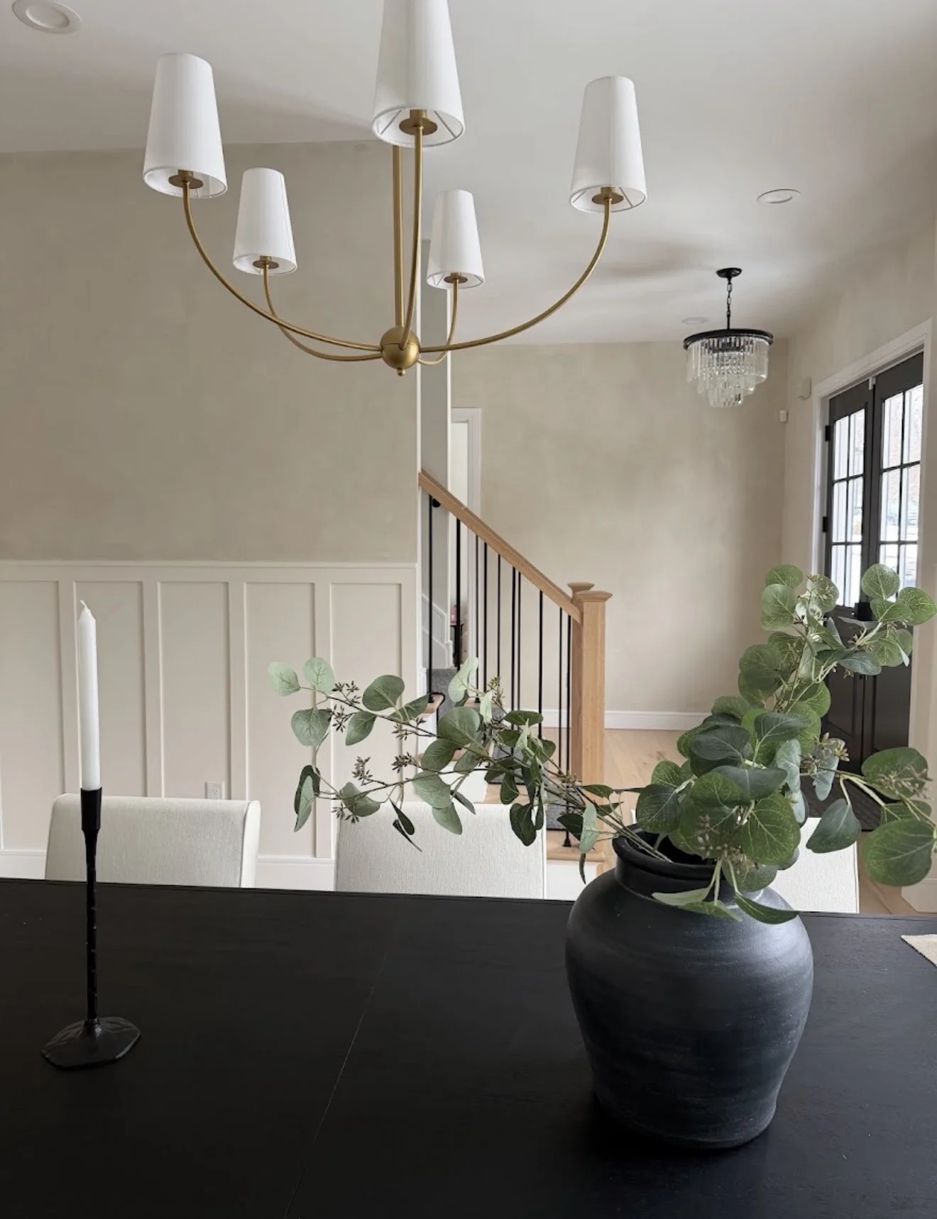 Warm white limewash dining room wall with brass chandelier and view into the limewashed entry hallway in Glen Rock NJ