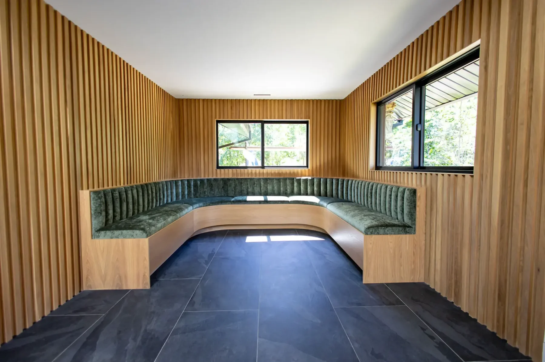Breakfast room with slat wood walls and curved green velvet banquette in Pompton Plains, NJ