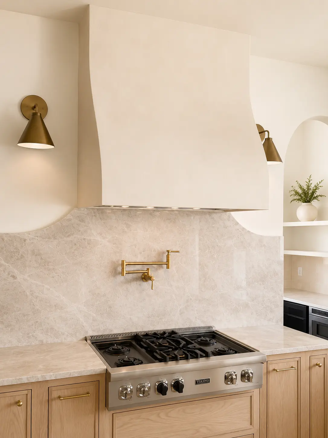 Curved cream plaster range hood with quartzite backsplash and brass sconces in Fairfield, NJ