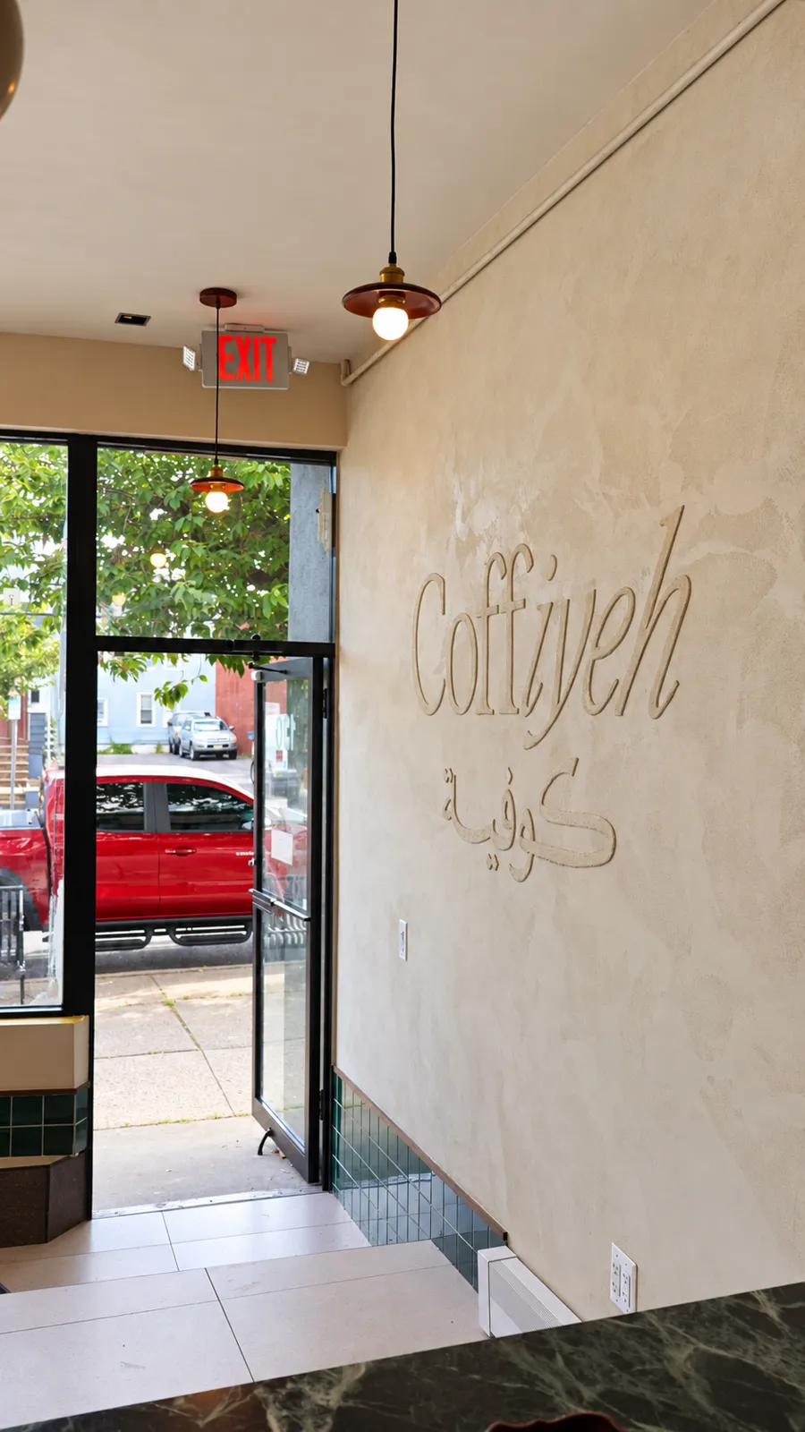 Limewash entry wall with raised Coffiyeh lettering in English and Arabic beside the storefront door at Coffiyeh coffee shop in Clifton, NJ