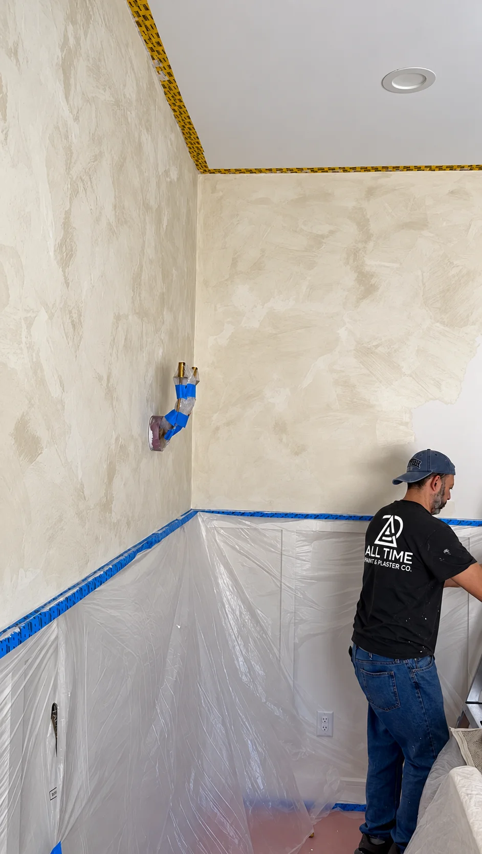 First coat of warm white limewash brushed across the corner walls of a Glen Rock NJ dining room, sconce wrapped in tape
