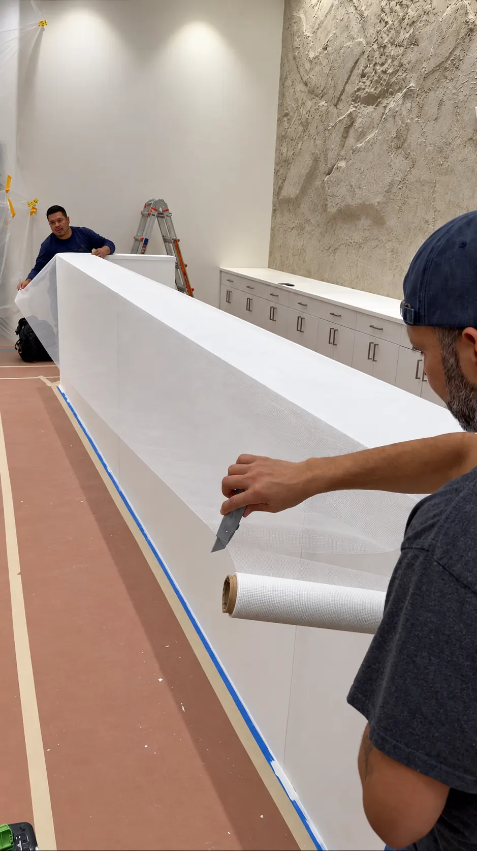 All Time Paint & Plaster crew wrapping and trimming reinforcement mesh over the custom microcement checkout counter at the Veiled flagship store in Clifton, NJ