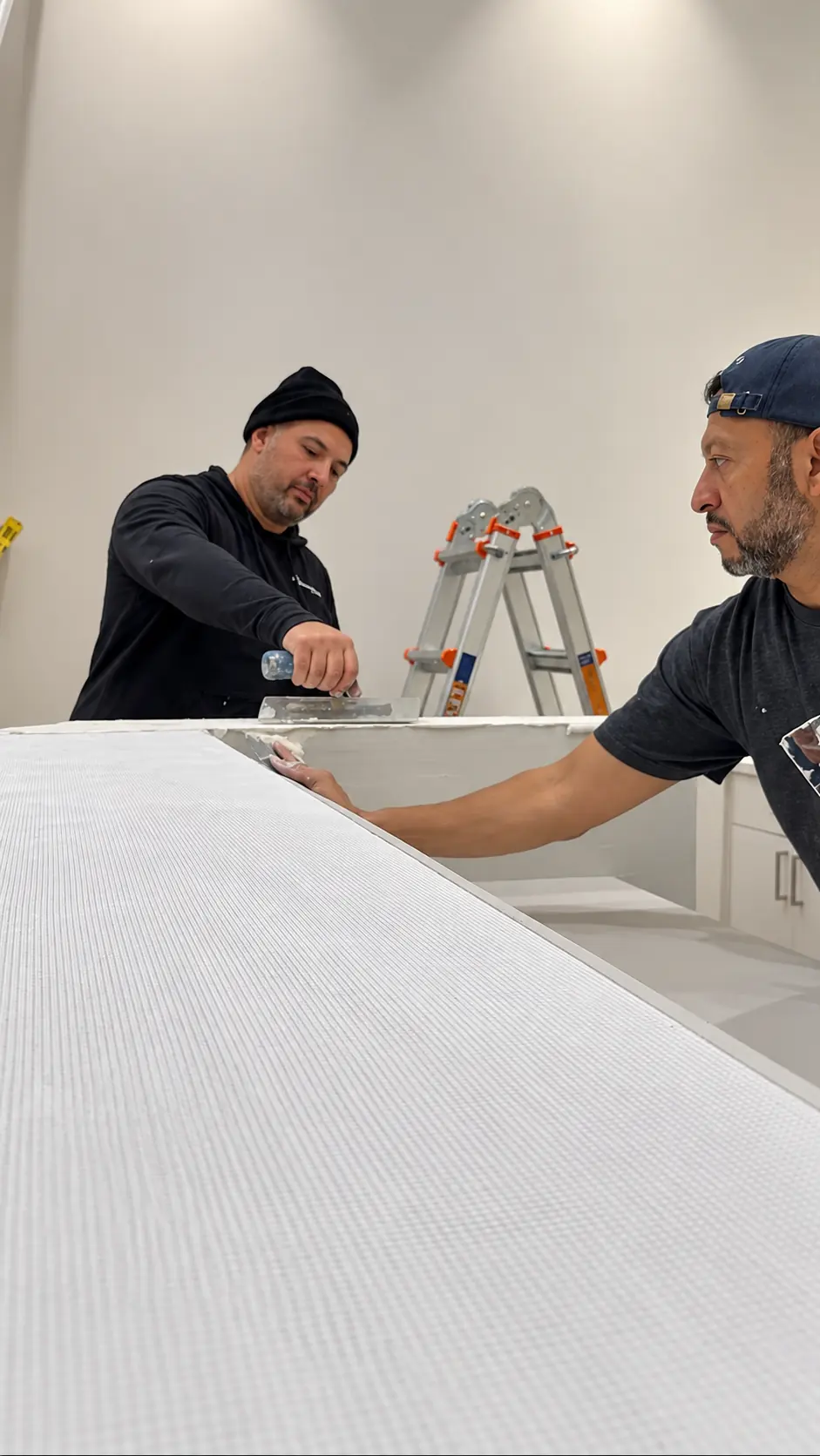 Two crew members embedding reinforcement mesh into the microcement base coat across the long horizontal counter surface in Clifton, New Jersey