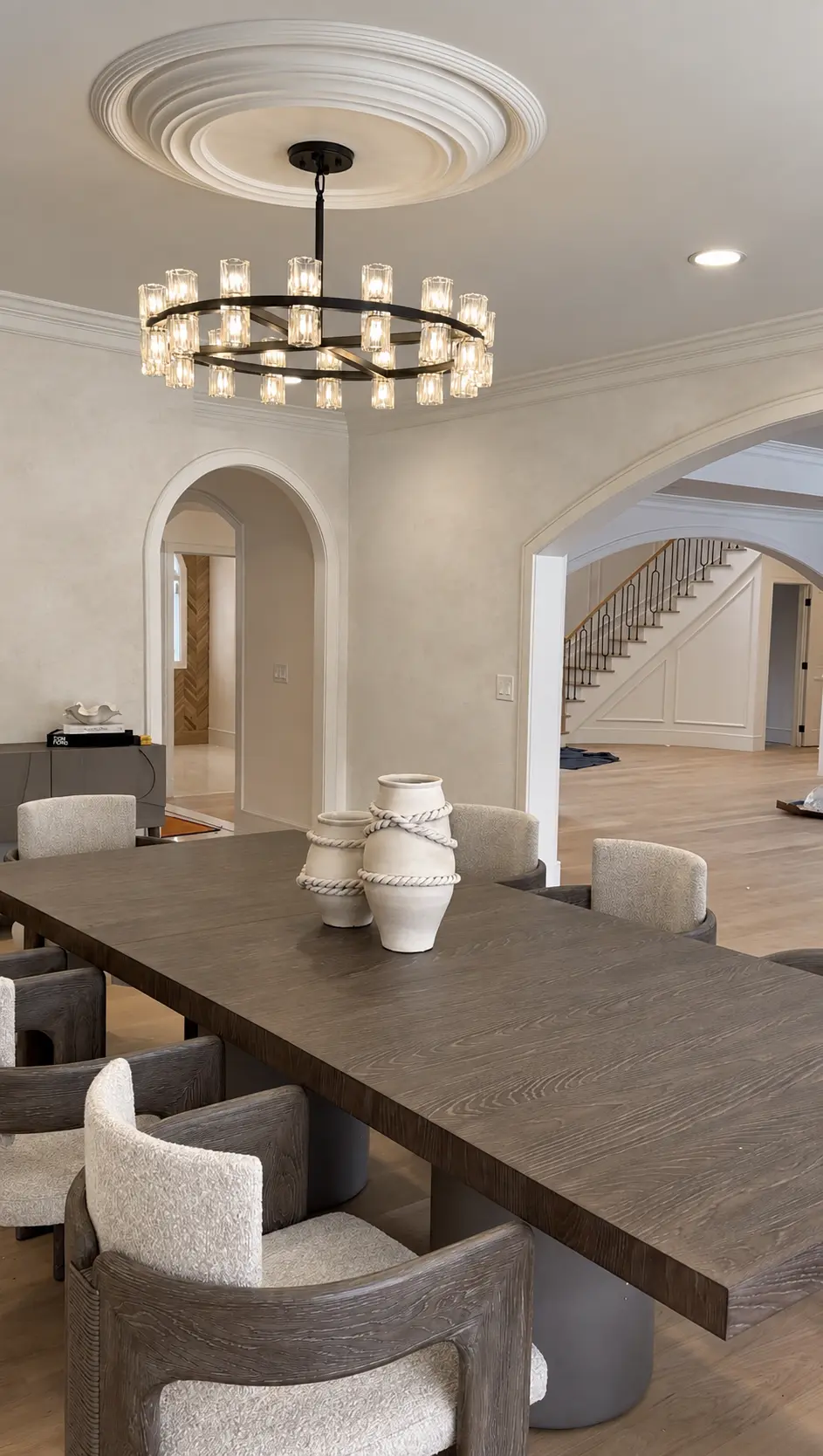 Limewashed dining room with arched openings, a ceiling medallion and a wide iron chandelier